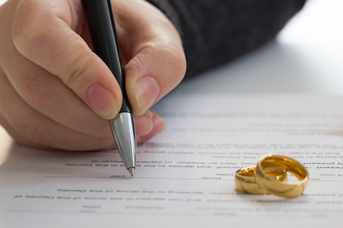 Hands of wife, husband signing decree of divorce, dissolution, canceling marriage, legal separation documents, filing divorce papers or premarital agreement prepared by lawyer. Wedding ring.