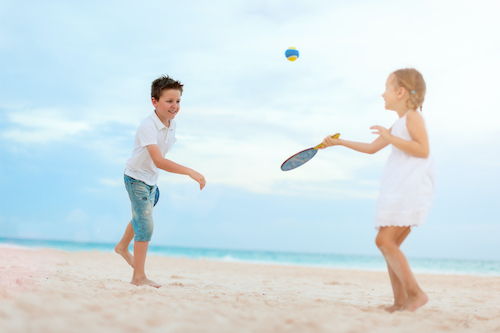 Little kids playing beach tennis on summer vacation