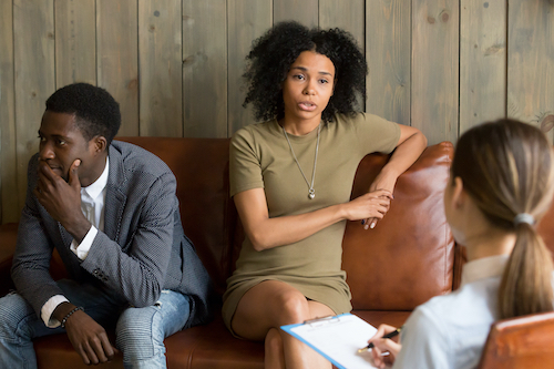 African frustrated wife talking to psychologist sitting on couch with husband, black unhappy woman sharing marital problems with counselor, family marriage therapy session, couple counseling concept